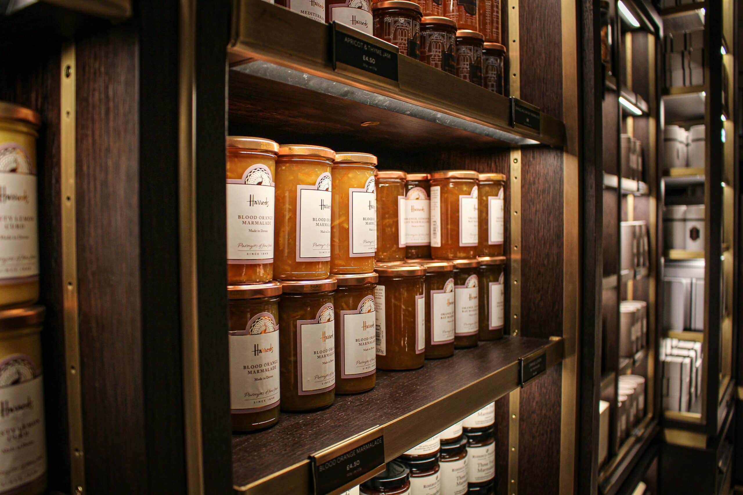 Jars of orange marmalade in a big cupboard on wooden shelves.